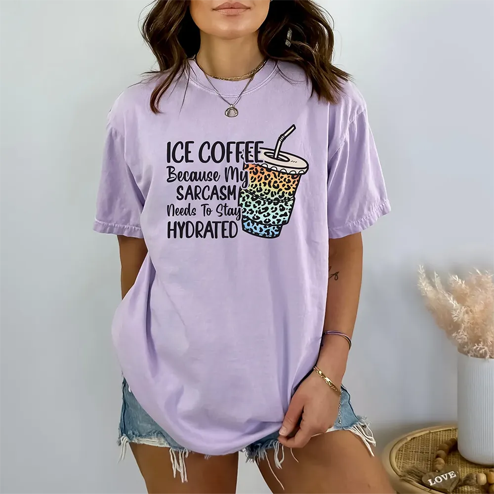 Model wearing a lavender t-shirt with UV DTF print that reads 'Ice Coffee Because My Sarcasm Needs To Stay Hydrated,' featuring a colorful leopard print iced coffee graphic, casual summer outfit.